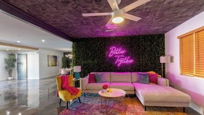 A modern living room with a sectional sofa, a colorful rug, and a neon sign on the wall.