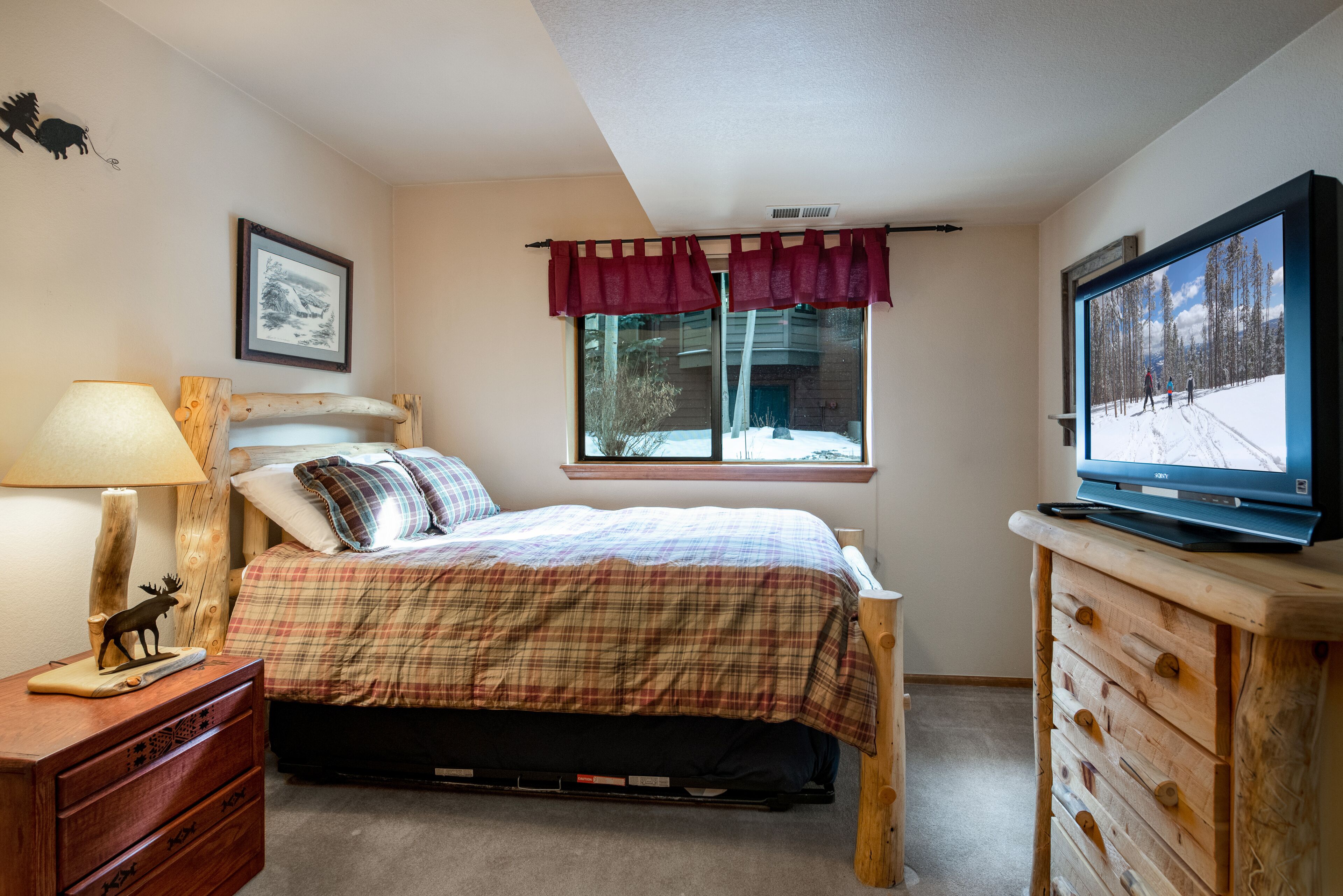 A bedroom with a bed, a dresser, a television, a window with curtains, and a wall-mounted picture.