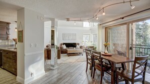 A spacious living area with a dining table and chairs, a sofa, and a large window offering a view of the outdoors.