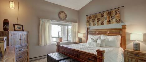 A bedroom with a wooden bed, a dresser, a window with curtains, a wall clock, and a decorative tapestry.