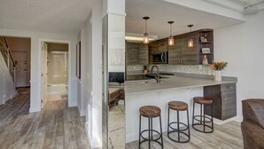 A modern kitchen with a large island, bar stools, pendant lighting, and a built-in microwave.
