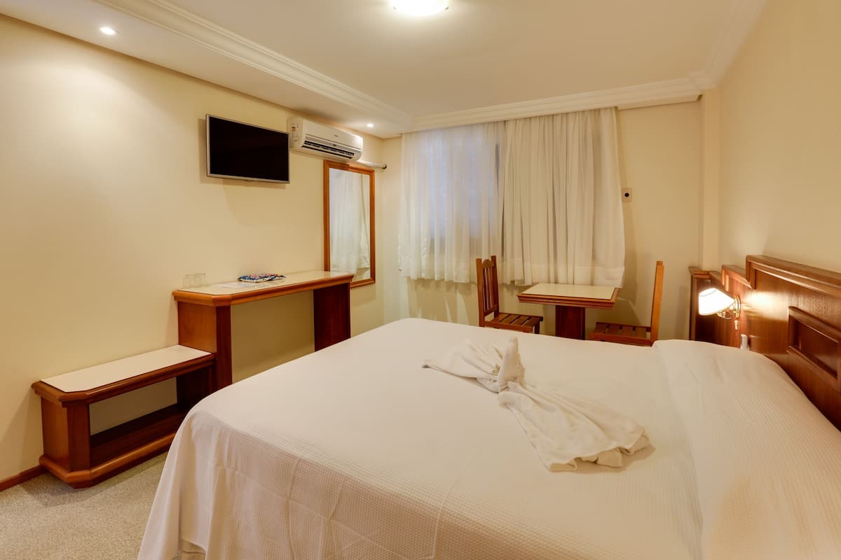 Ein Hotelzimmer mit Bett, Schreibtisch, Stuhl, Fernseher und Klimaanlage.
