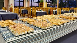 A buffet setup with various baked goods and a view of the evening sky through large windows. - Hotel San Isidro (Sao Gabriel)