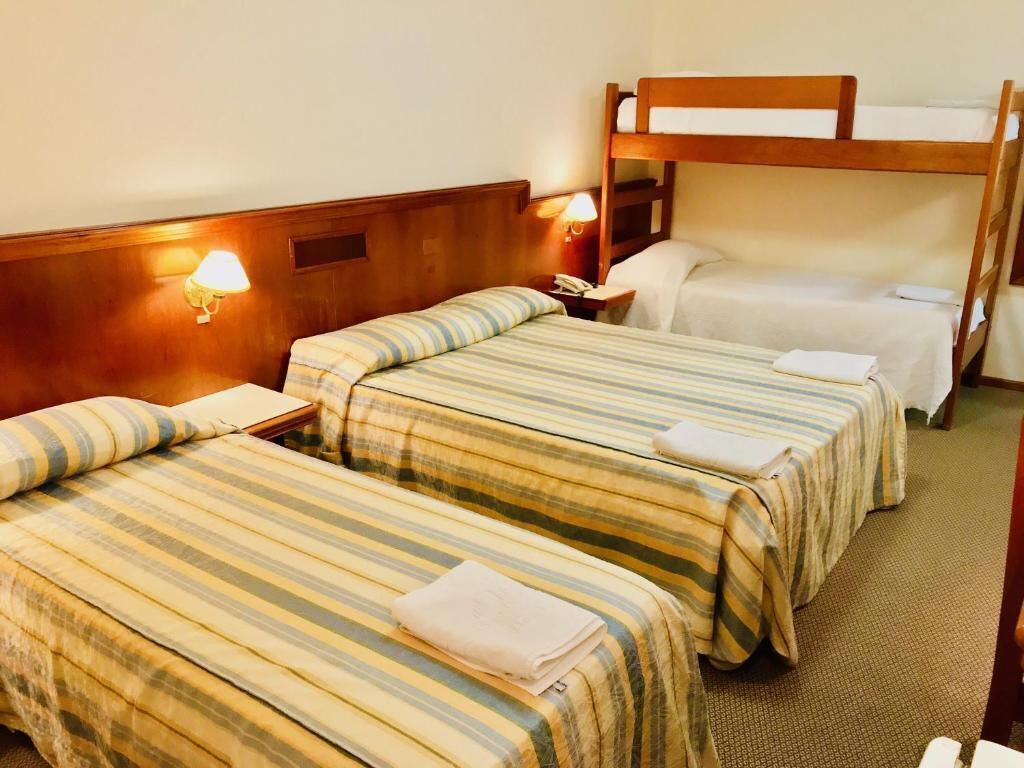 A hotel room with two single beds and a bunk bed, each with striped bedding. There are bedside lamps and a nightstand with a phone.