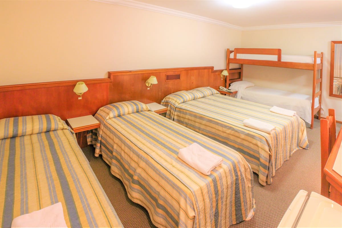 Ein Hotelzimmer mit vier Einzelbetten, einem Schlafsofa und einem Schreibtisch mit Lampe sowie einem kleinen Tisch.