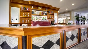 A reception area with a wooden counter, marble tiles, and shelves stocked with various liquor bottles. - Hotel San Isidro (Sao Gabriel)