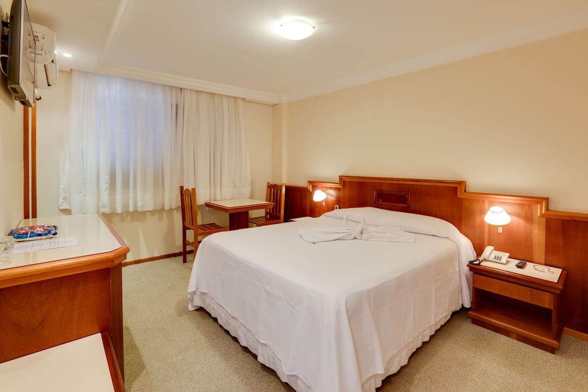 Ein Hotelzimmer mit einem großen Bett, Nachttischen, einem Schreibtisch und einem Sessel.