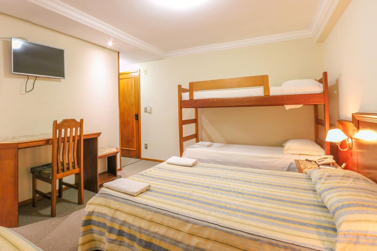 Ein Hotelzimmer mit einem Etagenbett, einem Schreibtisch mit Stuhl, einem Fernseher und einer Nachttischlampe.