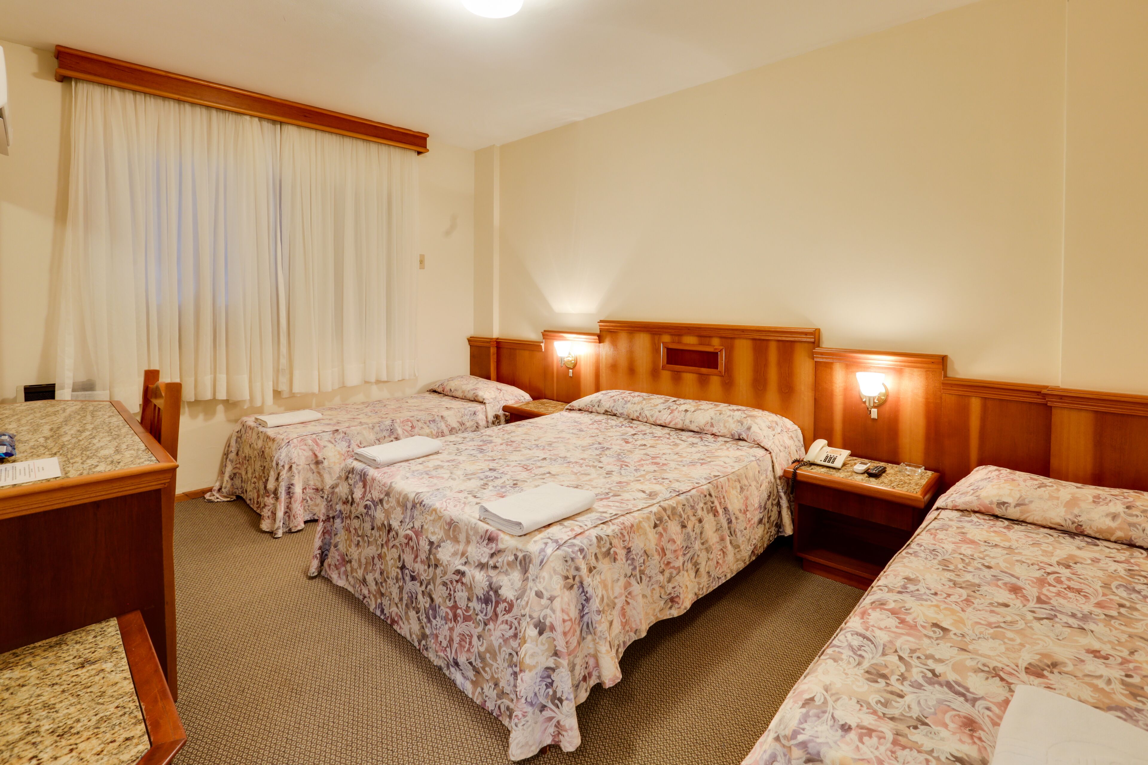 A hotel room with three beds, a desk, and a telephone.