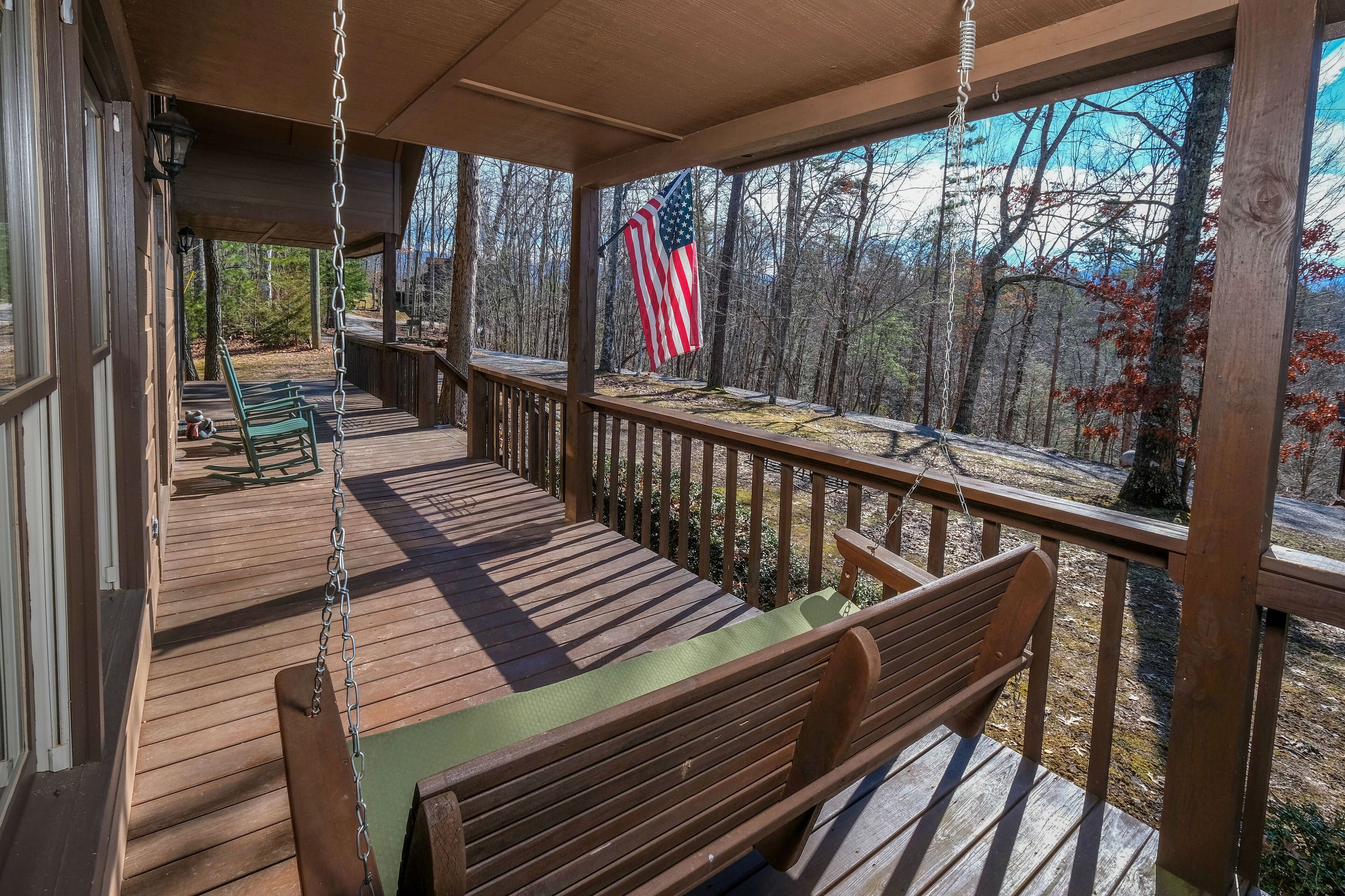 A wooden deck with a swing, an American flag, and a view of a forest.