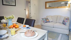 A dining area with a table set for breakfast, including oranges, a loaf of bread, and a pitcher of flowers. - Fermain Apartment - Spacious cosy duplex apartment - Sleeps 5 (Filey)
