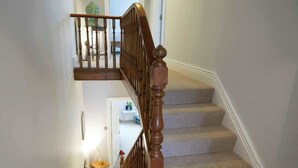 A wooden staircase with a handrail, carpeted steps, and a small table with a plant at the bottom landing. - Fermain Apartment - Spacious cosy duplex apartment - Sleeps 5 (Filey)