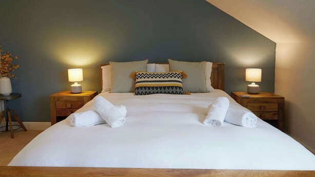 A large bed with white linens, two bedside tables with lamps, and a patterned pillow. - Fermain Apartment - Spacious cosy duplex apartment - Sleeps 5 (Filey)