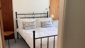 A bedroom with a bed, pillows, a nightstand, a chair, and a painting on the wall. - Sunbeam Cottage - 3 bedroom traditional cottage - Straight off the beach (Filey)