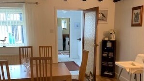 A dining area with a wooden table and chairs, a bookshelf, and a view into the kitchen. - Sunbeam Cottage - 3 bedroom traditional cottage - Straight off the beach (Filey)