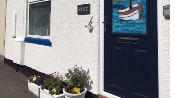 A white building with a dark blue door, a small window, and a number plate reading "93". - Sunbeam Cottage - 3 bedroom traditional cottage - Straight off the beach (Filey)