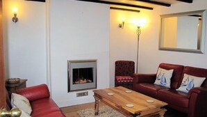 A living room with a fireplace, red leather sofa, wooden coffee table, and a red armchair. - Sunbeam Cottage - 3 bedroom traditional cottage - Straight off the beach (Filey)