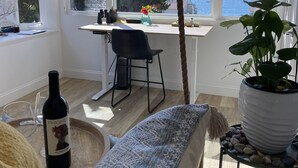 A cozy room with a large window overlooking the sea, a dining table with chairs, a potted plant, and a bottle of wine on the floor. - Gorgeous Oceanview Home! Steps to Beach, Pool & Pickleball (Encinitas)