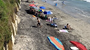 A beach with people sunbathing and swimming, umbrellas, and a cliff with vegetation. - Gorgeous Oceanview Home! Steps to Beach, Pool & Pickleball (Encinitas)