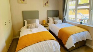 A bedroom with two beds, a hanging light fixture, and a window with curtains. - Hollicarrs - Wildflower Lodge (York)
