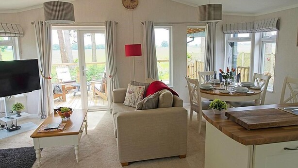 A spacious living room with a sofa, a dining table set for four, and a TV on a stand. - Hollicarrs - Wildflower Lodge (York)