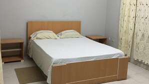 Un dormitorio con una cama de madera, dos mesitas de noche, un estante pequeño y una cortina estampada.