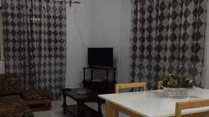 Una sala de estar con televisor, una mesa de comedor y cortinas estampadas.