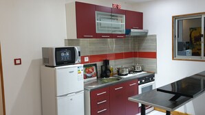 Una cocina compacta con microondas, refrigerador, estufa y armarios rojos.