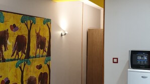 Un pasillo con un cuadro llamativo de elefantes y árboles, un refrigerador blanco y una puerta de madera.