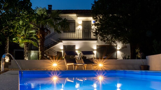 A swimming pool with lounge chairs and a two-story building with a balcony in the background.