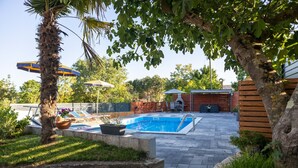 A swimming pool area with a tiled deck, lounge chairs, and a palm tree.