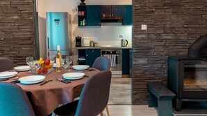 A modern dining area with a stone wall, a built-in kitchen with teal cabinets, and a wood-burning stove.