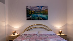 A bedroom with a bed, two bedside lamps, and a painting of a mountain landscape.