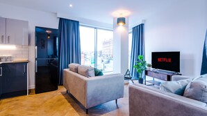 A modern living room with a sofa, a TV displaying 'NETFLIX', and a kitchen area.