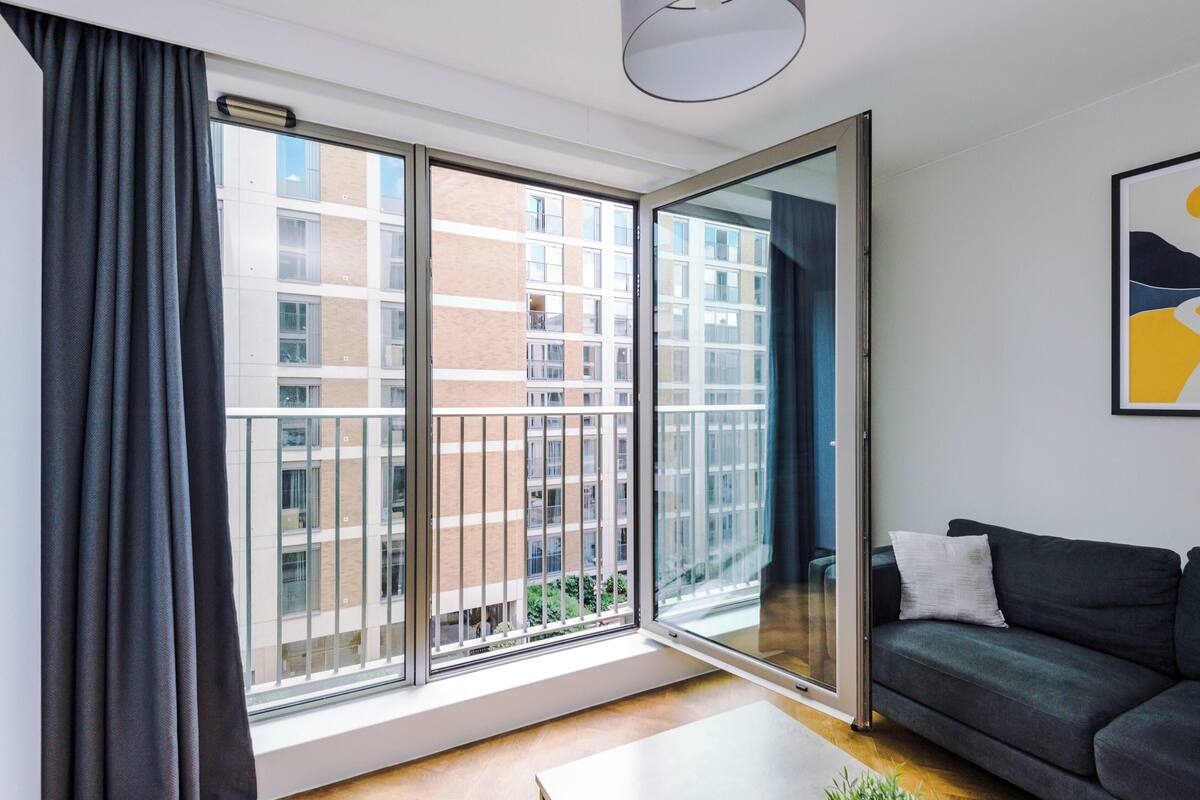 A modern living room with a large sliding glass door leading to a balcony, a dark grey sofa, and a minimalist decor style.