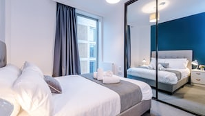 A modern hotel room with a large bed, a bedside table with a lamp, and a mirror reflecting the room.