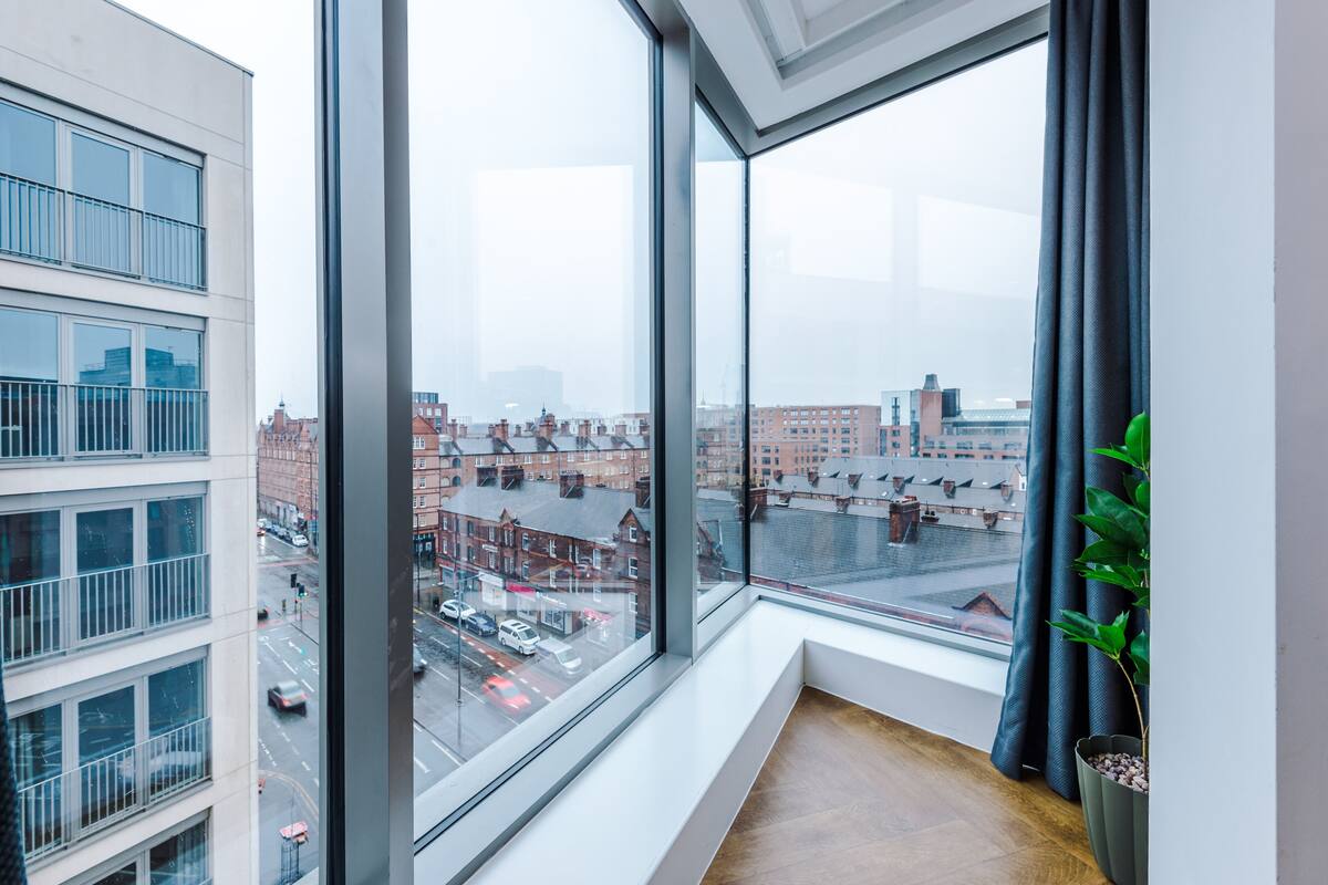 A modern room with a large window offering a city view, a potted plant, and a wooden floor.
