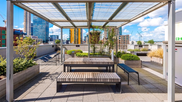 An outdoor seating area with benches and planters, surrounded by a metal pergola structure.