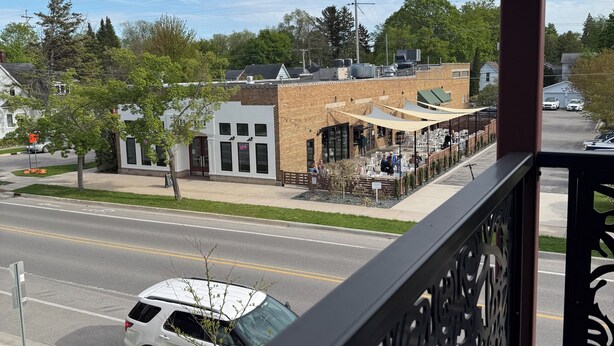 A balcony with a view of a street, a restaurant, and a white car parked on the side. - Traverse City, West side of downtown, Sleeps 6, Slabtown area (Traverse City)