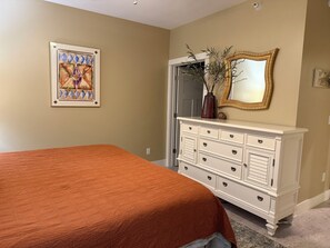 A bedroom with a bed, dresser, mirror, and artwork on the wall.