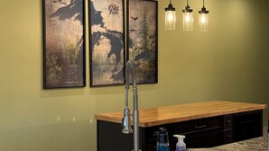 A kitchen with a granite countertop, a stainless steel faucet, a wooden bench, and two wall-mounted light fixtures. - Traverse City, West side of downtown, Sleeps 6, Slabtown area (Traverse City)