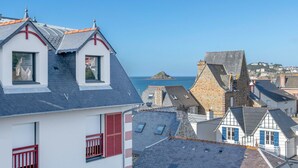 Un poble costaner amb edificis de pedra tradicionals, una església destacada amb una creu vermella i vista al mar.