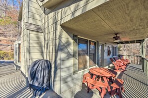 Un patio techado al aire libre con mesas y sillas de madera, un ventilador de techo y una parrilla.
