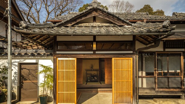 Een traditioneel Japans gebouw met een pannendak, houten schuifdeuren en een plant in de entree.