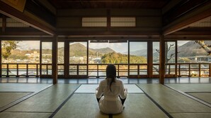 Een persoon mediteert in een kamer met tatami matten, grote ramen en traditionele houten balken.
