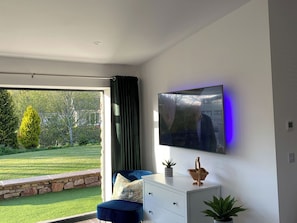 A modern living room with a large TV, a sofa, a stone wall, and a view of a garden.