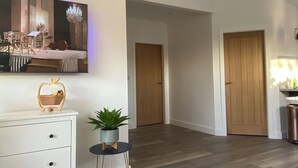 Een moderne woonkamer met een flatscreen televisie, een houten deur, een klein rond tafeltje met een plant en een witte kast.