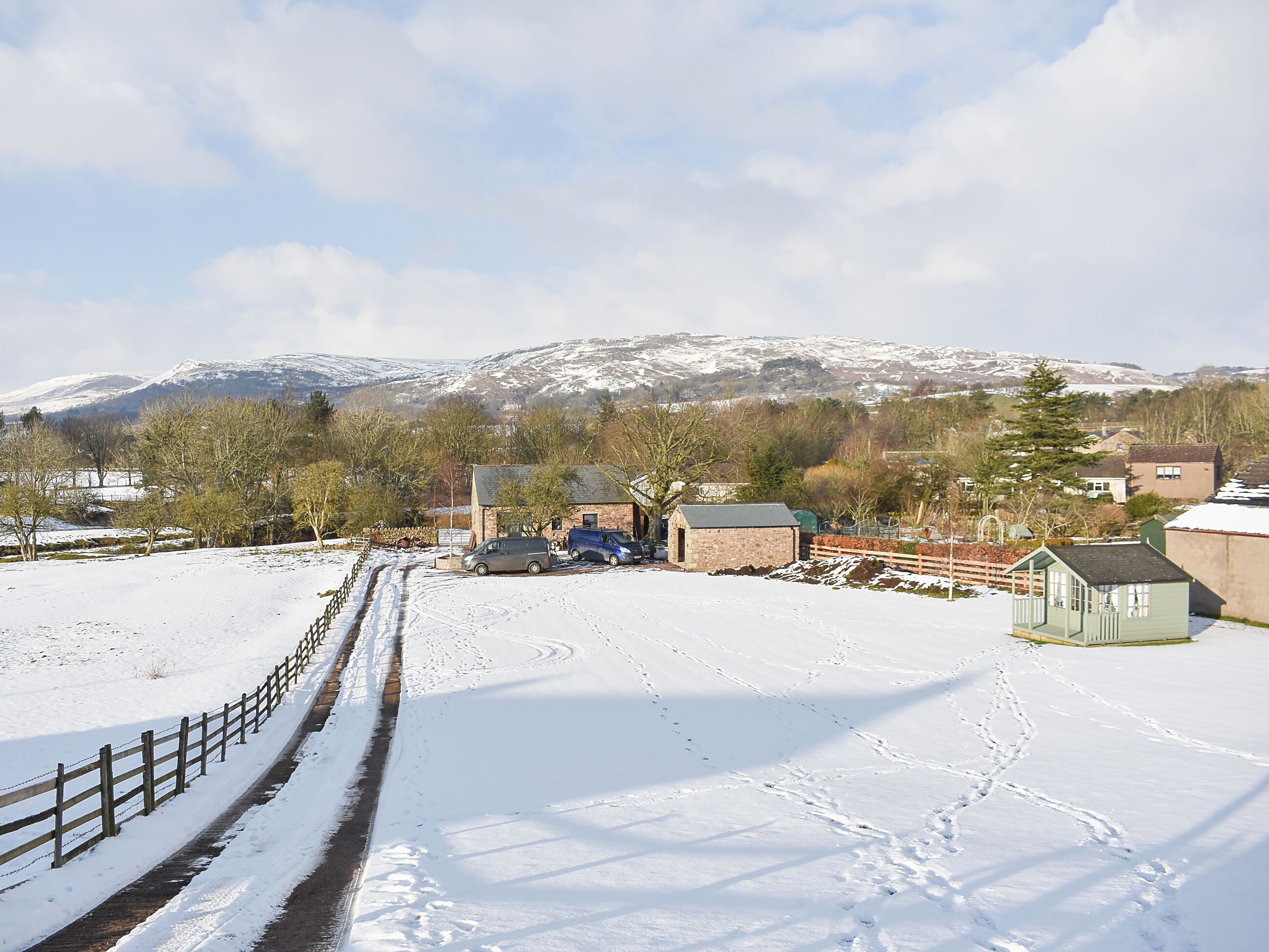 A rural landscape with a snow-covered ground, a wooden fence, and a small building.