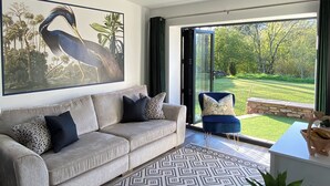 Een moderne woonkamer met een groot schilderij, een bank, een stoel en uitzicht op een tuin door een glazen deur.