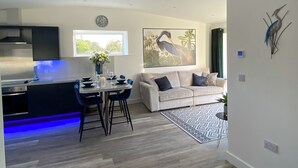 Een moderne keuken met een ingebouwde kookplaat, een eethoek met een tafel en stoelen, een bank en een groot schilderij van een vogel aan de muur.